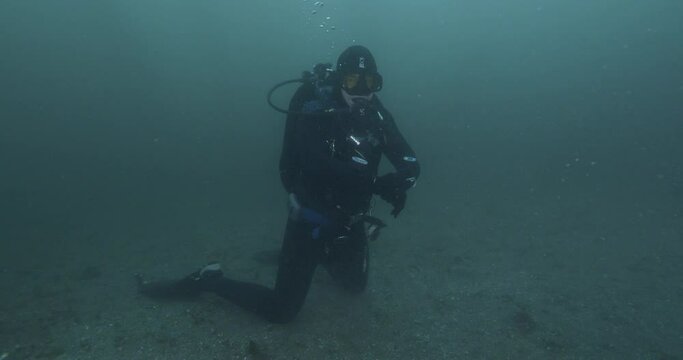 Scuba diver kneeling on seabed poor visibility.