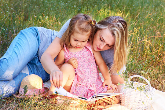 Mother read book to little daughter outdoor in park over green grass background Family concept 