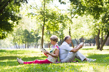 senior couple read bookssitting on the grass in the park on a summer day