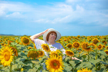Fototapeta na wymiar adult european woman in a white hat on a field with sunflowers, summer sunny day in the countryside