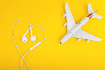View from above at the plane and headphones in the form of heart on the yellow desk.