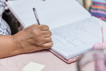 Pessoa fazendo uso de caneta para escrever em caderno.