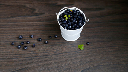 Fototapeta na wymiar Heap of American blueberries scattered from a white bucket, on a black wooden background