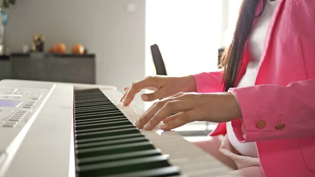 Pregnant young woman plays on a white digital piano for the baby.