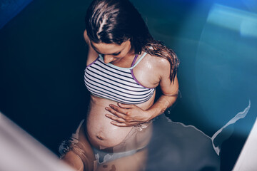 Beautiful pregnant woman floating in tank filled with dense salt water used in meditation, therapy, and alternative medicine.