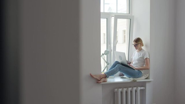 Young woman blogger sitting in room on windowsill calling video call speaking. Distance learning
