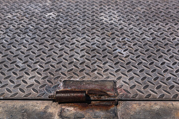 Diamond pattern rusty metal plate. Weathered steel plate with rusty hinge