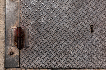Diamond pattern rusty metal plate. Weathered steel plate with rusty hinge