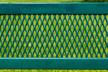 Green metal bench with diamond grid pattern. Weathered park bench with green grass background. 