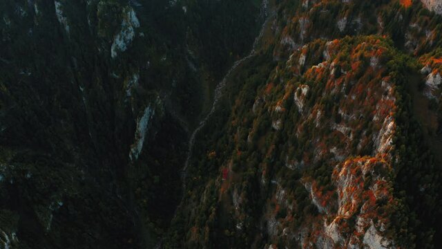 Aerial view over the mountain road. Video from drone flying over forested and cliffs slopes of mountains. Sunset time in Romania, travel background, 4k