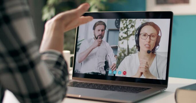 View from shoulder of mature woman having business meeting with male and female partners on laptop. Colleagues keeping social distance and talking with each other online.