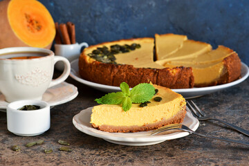 Slice of pumpkin cheesecake with a cup of coffee on a concrete background.