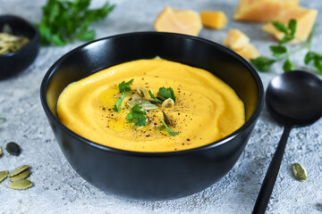 Pumpkin puree soup with cream and pumpkin seeds on a concrete background.