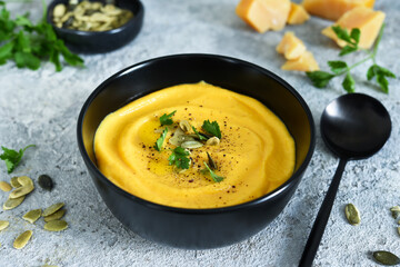 Pumpkin puree soup with cream and pumpkin seeds on a concrete background.