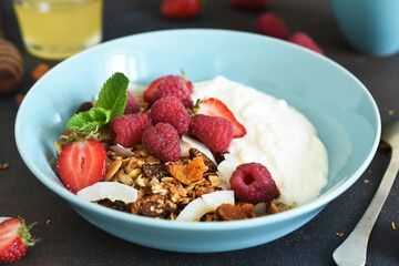 Classic breakfast - granola with honey, coconut, yogurt and berries on a black background.