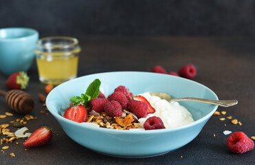 Classic breakfast - granola with honey, coconut, yogurt and berries on a black background.