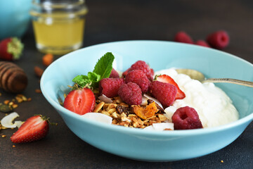 Classic breakfast - granola with honey, coconut, yogurt and berries on a black background.