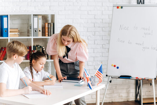 English class. Two schoolchildren, a boy and a girl, are sitting at a desk in an English lesson, and a young woman teacher helps them complete the task