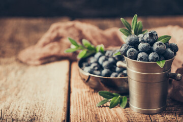 Blueberries in metal bowl on a wooden background.