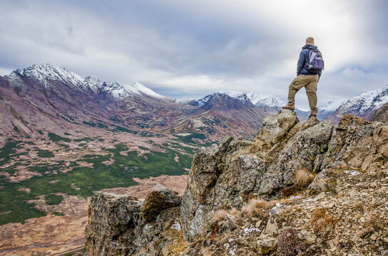 Adventurous man standing on the side of a mountain looking at the open landscape on a cloudy day.