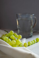 green grapes on white wood, behind a cup of water