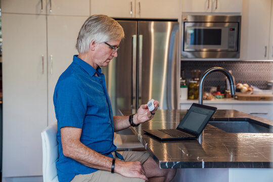Senior man working from home kitchen checking temperature for fever with digital thermometer