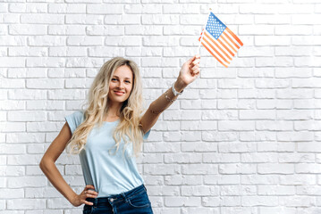 A Girl with the USA flag. Young attractive caucasian woman in a casual clothes, is posing with usa flag near a white wall indoors and smiling