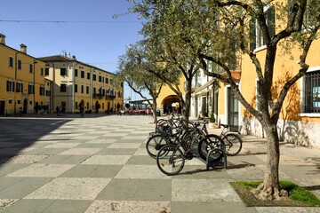 Fototapeta na wymiar View of the main square of the old town on the shore of Lake Garda with bicycles parked under a row of olive trees, Lazise, Verona, Veneto, Italy