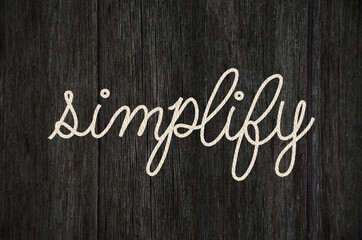 close up of word simplify rope text design on black wood grain 
