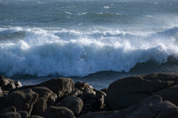 White surf wave on ocean, on a windy day with rocks in foreground.