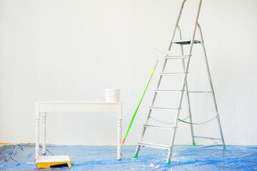 Tools for painting walls: a stepladder, roller, tray, bucket of paint, a brush on the floor with a...