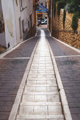 Fototapeta na wymiar Narrow alley with two tracks for car wheels and stairs in the middle, Polop de Marina, Spain