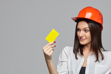 a girl in an orange construction helmet, with a business card in her hand on a white background. the concept of advertising..