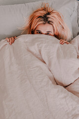 Young woman is relaxing in bed. Day off. Bedtime. Early morning light. White, beige, grey. Light and bright. Morning ritual. Apartment lifestyle living. Cozy bed linen. Taking a nap, sleep. Relaxed