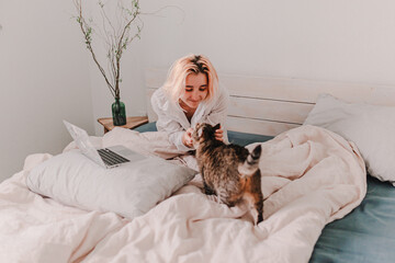 Young woman is relaxing in bed. Day off. Bedtime. Early morning light. White, beige, grey. Light and bright. Morning ritual. Apartment lifestyle living. Cozy bed linen. Soft pillow and comforter.