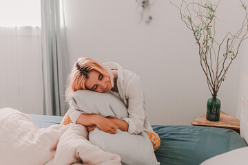 Young woman is relaxing in bed. Day off. Bedtime. Early morning light. White, beige, grey. Light and bright. Morning ritual. Apartment lifestyle living. Cozy bed linen. Soft pillow and comforter.