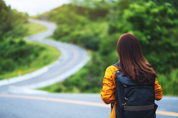 Rear view image of a female traveler with backpack walking along a mountain road