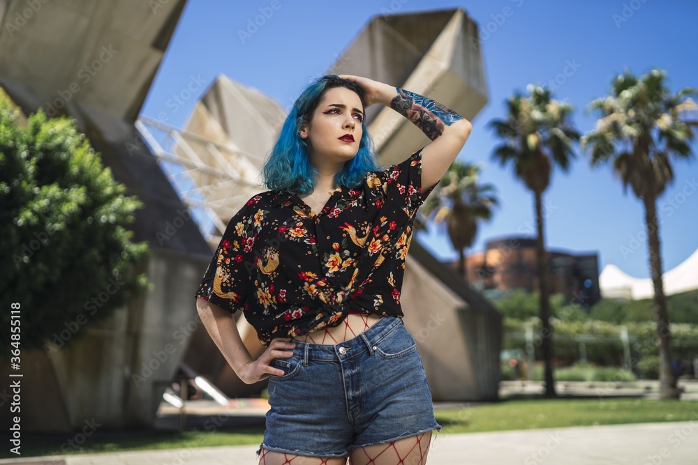 Sticker Shallow focus of a young female with blue hair wearing shorts in a park under the sunlight