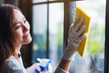 A young woman wearing protective glove cleaning the window for housework concept