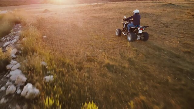 Riding quad bike. Man in protective equipment and helmet, drifting on his ATV at sunset. Aerial footage. High quality 4k footage