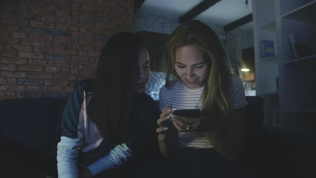 Happy friends sitting on sofa and looking at screen of mobile phone or smartphone. Quarantine using modern technology. Connecting through social networks or messages during epidemic. phubbing concept.