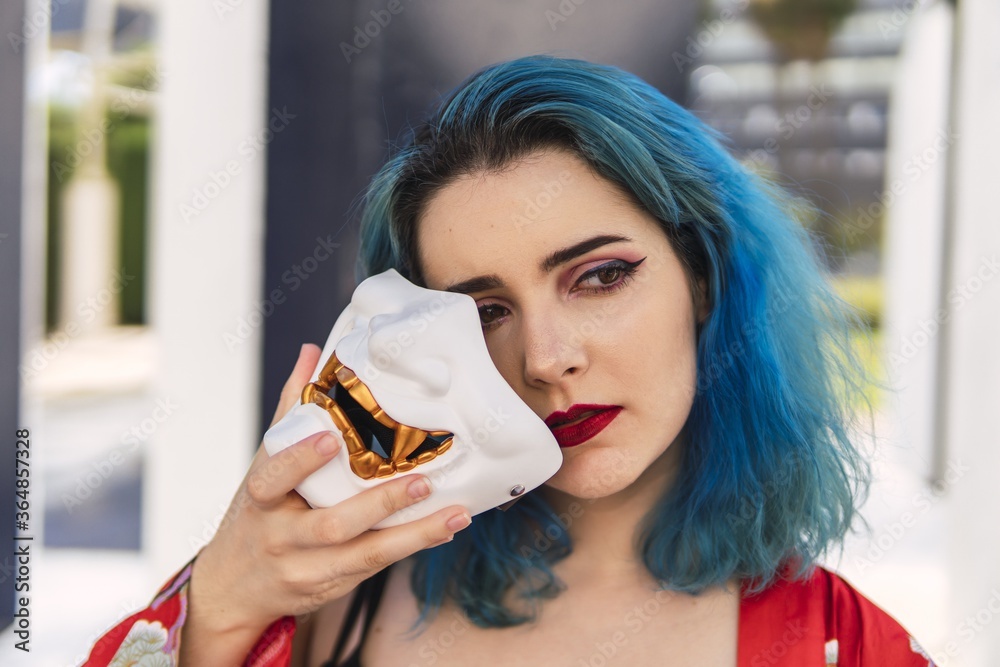 Wall mural european female with blue hair and red lipstick holding a mask