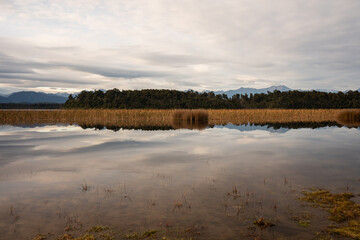 Fototapeta premium Jezioro Mahinapua na Wyspie Południowej Nowej Zelandii w spokojny dzień z odbijającymi się drzewami i górami
