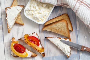A breakfast, top view. Slices of toasted bread with white soft cheese and fried bell peppers.