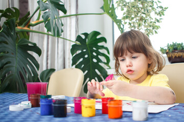 Little caucasian girl paints small toy figures in home interior. A cute three year old child is engaged in creativity.