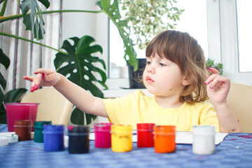 Little caucasian girl paints small toy figures in home interior. A cute three year old child is engaged in creativity.