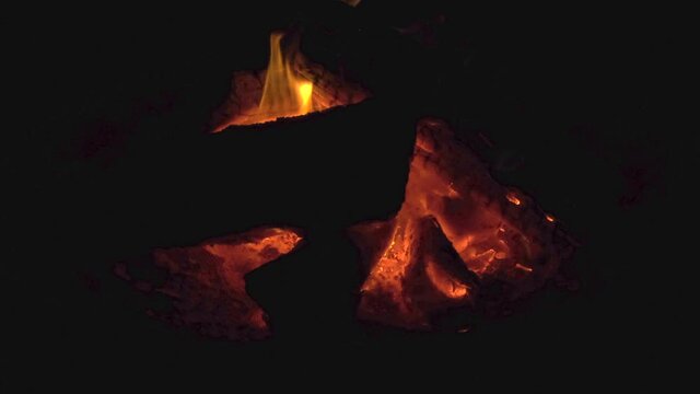 Time lapse: sensational zen scene of red embers and fire flames burning wood logs in firepit on dark black evening, static close up