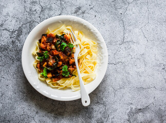 Tagliatelle pasta with eggplant, tomatoes, spinach vegetarian sauce on a grey background, top view