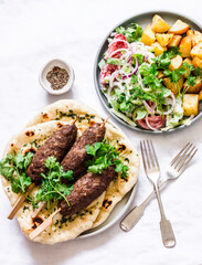 Mediterranean style lunch table. Meat kebab, garlic herb naan, yogurt dressing vegetable salad, roasted potatoes - delicious lunch, tapas, snack in the  on a light background, top view