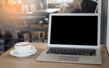 Fototapeta premium Modern technology and communication concept. Close up view of open notebook computer, and mug of cappuccino resting on wooden table,